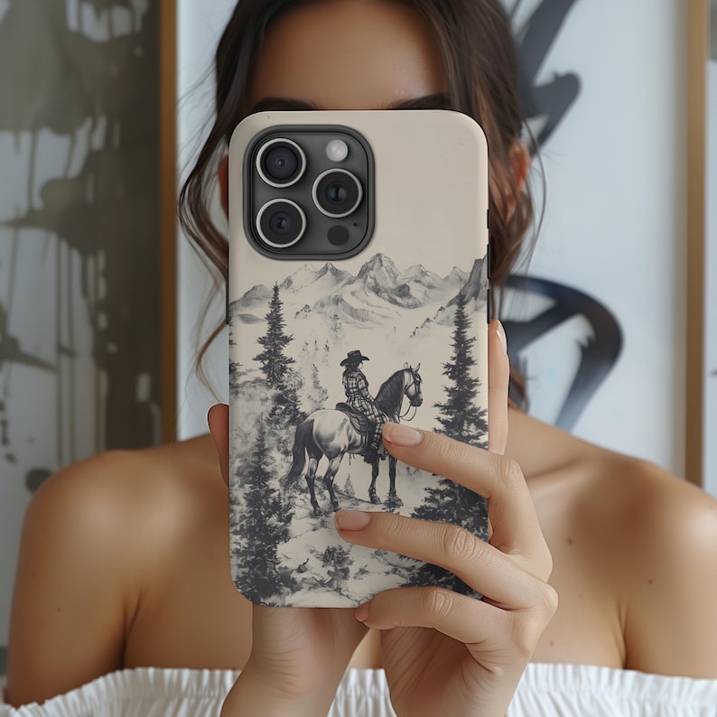 May include: A white phone case featuring a black and white illustration of a person riding a horse in a mountainous landscape. The case has a camera lens cutout and a white background.