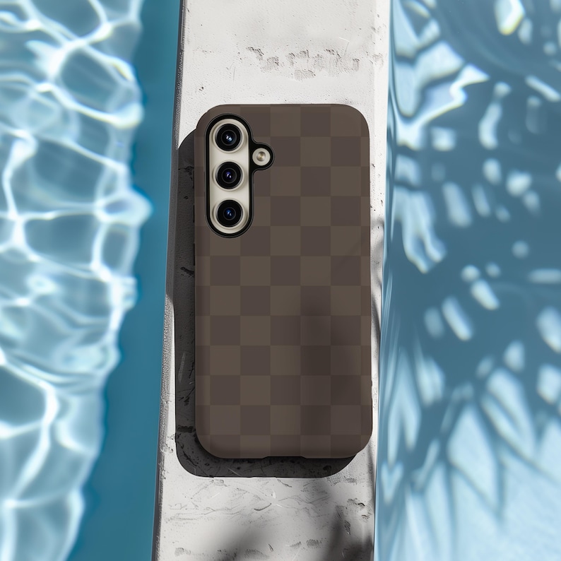 May include: A brown phone case with a checkered pattern. The case has a camera lens with three holes.