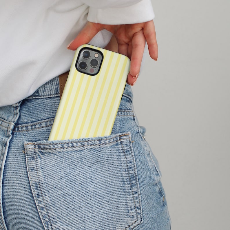 Pode incluir: Uma capa de telefone listrada amarela e branca em um bolso traseiro de jeans azul.