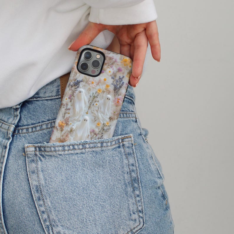 K&ouml;nnte beinhalten: Eine Handyh&uuml;lle mit floralem Muster und kleinen wei&szlig;en Geisterfiguren. Die H&uuml;lle befindet sich in der Tasche einer blauen Jeans. Die Handyh&uuml;lle hat eine Multi-Kamera-Linse.