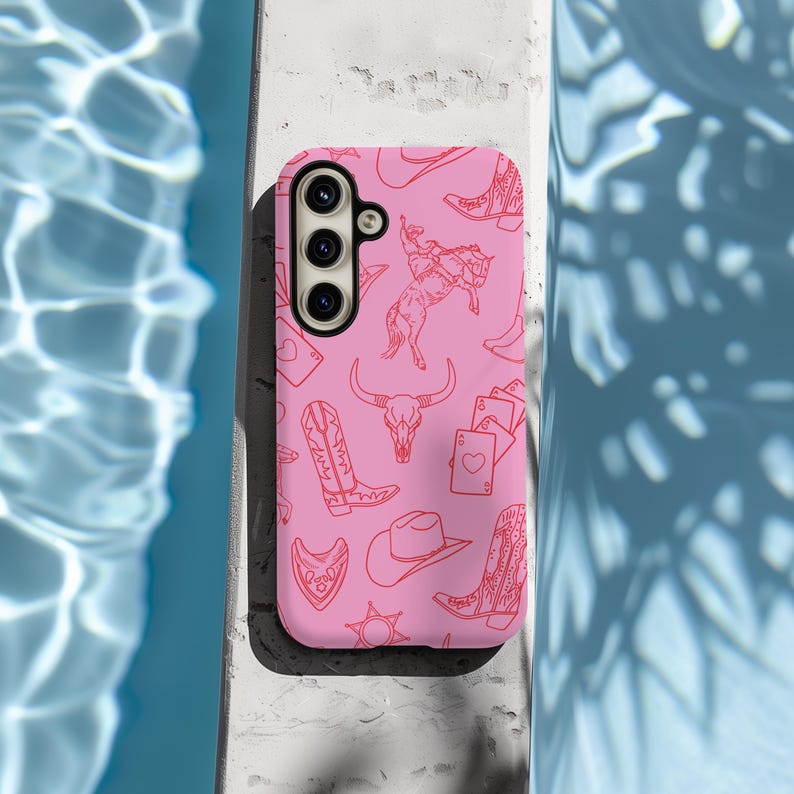 May include: Pink phone case with a pattern of cowboy boots, hats, horses, and playing cards. The case has a cutout for a triple camera lens.