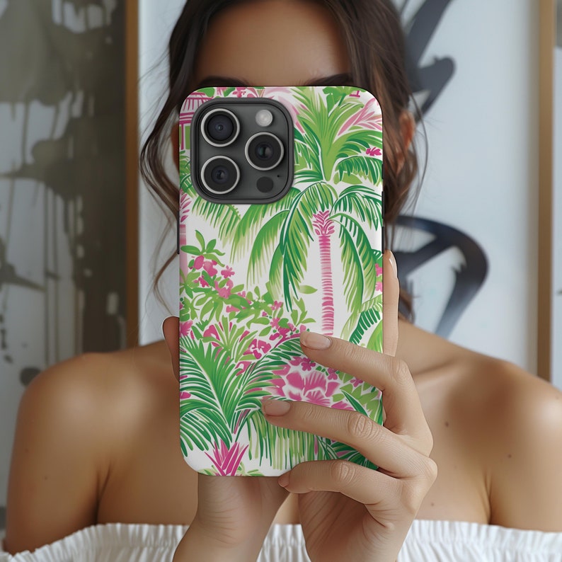 May include: A white iPhone case with a tropical print featuring palm trees and pink flowers. The case has a cutout for the camera lens.