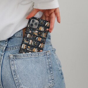 Pu&ograve; includere: Una custodia per telefono nera con un design a libreria con libri e fiori. La custodia &egrave; in una tasca posteriore di jeans blu.
