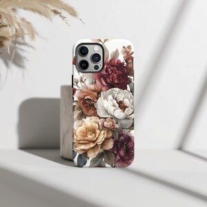 May include: A white iPhone case featuring a watercolor floral design. The design includes a variety of flowers in shades of burgundy, peach, cream, and yellow. The case has a glossy finish and a camera cutout.