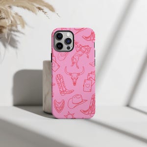 May include: Pink iPhone case with a red line drawing pattern of cowboy boots, hats, a skull, and playing cards.