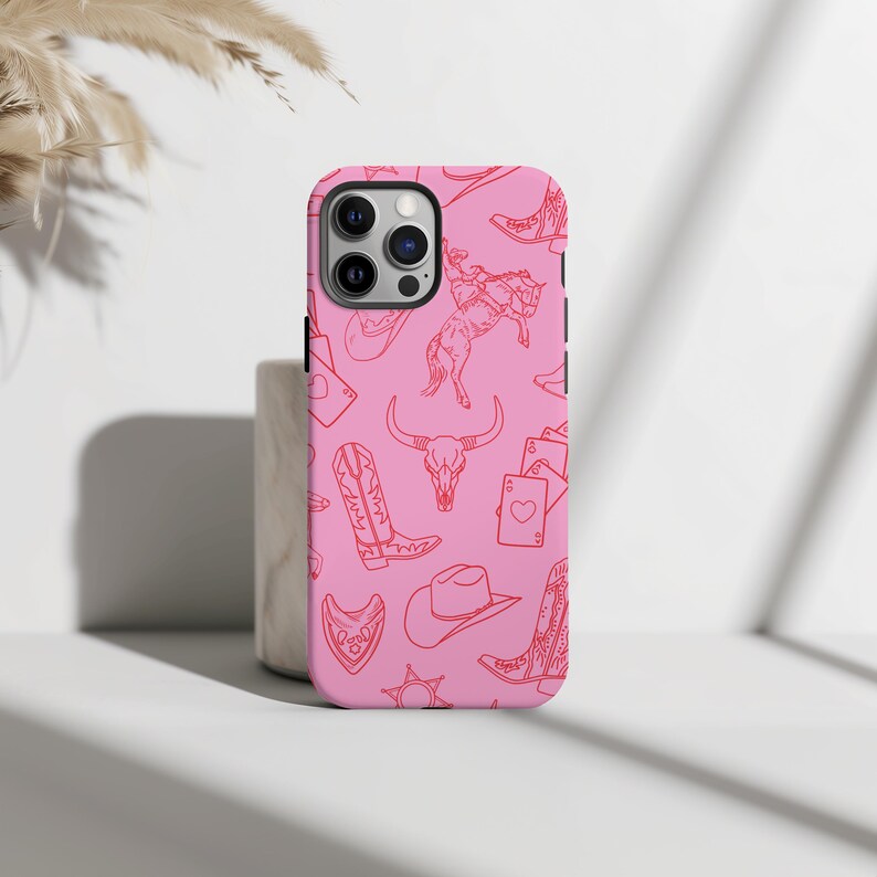 May include: Pink iPhone case with a red line drawing pattern of cowboy boots, hats, a skull, and playing cards.