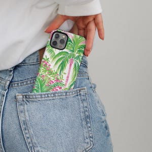 May include: A white phone case with a tropical print featuring palm trees and pink flowers. The case is in a back pocket of blue jeans.