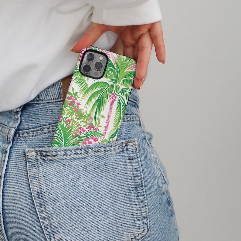 May include: A white phone case with a tropical print featuring palm trees and pink flowers. The case is in a back pocket of blue jeans.