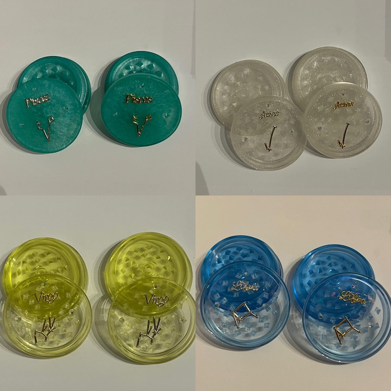 May include: Four sets of two clear plastic grinders with zodiac symbols and names. The grinders are in turquoise, white, yellow, and blue.