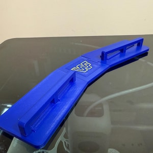 May include: A blue plastic object with the letters "WF" in gold. The object has a rectangular base with raised edges and a curved top with a handle. The object is on a reflective surface.