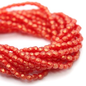 Puede incluir: Primer plano de hebras de cuentas facetadas de color rojo anaranjado. Las cuentas tienen un brillo metálico y están ensartadas, creando un efecto texturizado y en capas. Las cuentas probablemente se utilizan para la fabricación de joyas o manualidades.