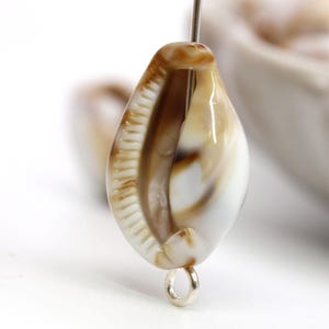 May include: A brown and white seashell with a silver loop attached to the bottom. The shell has a smooth, glossy finish and a natural, organic shape.