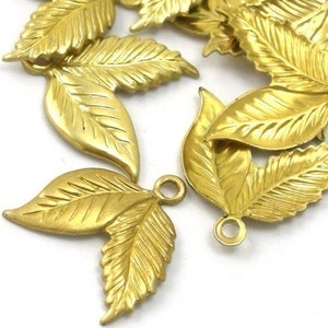 May include: A group of gold-colored metal leaf charms with a textured surface. Each charm has a small loop for attaching to jewelry or other crafts.