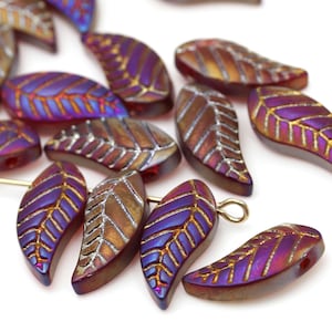 May include: A selection of iridescent leaf-shaped beads in shades of purple, gold, and brown. The beads have intricate veining and a hole for threading. These beads are suitable for jewellery making or other craft projects.