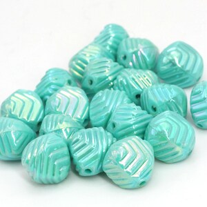 May include: A collection of turquoise-colored beads with a textured, geometric design. Each bead has a hole for stringing and a pearlescent sheen. The beads are clustered together against a white background.
