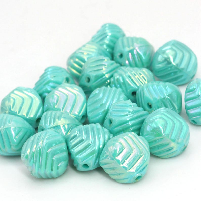 May include: A collection of turquoise-colored beads with a textured, geometric design. Each bead has a hole for stringing and a pearlescent sheen. The beads are clustered together against a white background.