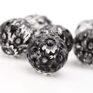 May include: Close-up of black metal beads with a floral design. The beads have a shiny finish and are perfect for jewelry making.