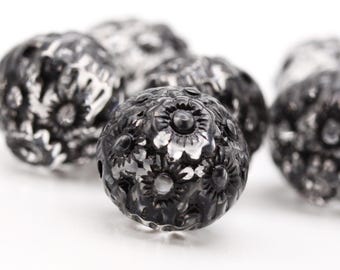Puede incluir: Primer plano de cuentas de metal negro con un diseño floral. Las cuentas tienen un acabado brillante y son perfectas para la elaboración de joyas.