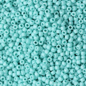 Può includere: Un'immagine ravvicinata di una grande quantità di piccole perline rotonde di colore turchese. Le perline sono tutte della stessa dimensione e forma, e sono disposte in uno schema casuale.