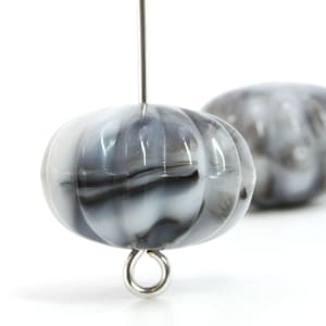 May include: Close-up of two gray and white marbled glass pumpkin beads. The beads are strung on a silver wire and have a silver loop at the bottom. The beads are round with vertical grooves, resembling a pumpkin.