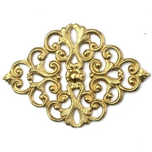 Puede incluir: Adorno de metal dorado filigranado con forma de diamante y un intrincado diseño de volutas.