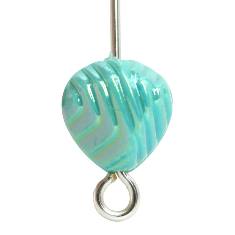 May include: A close-up of a teal glass bead with a textured, leaf-like design. The bead is suspended by a silver-colored metal loop and a straight pin. The bead has a pearlescent sheen.