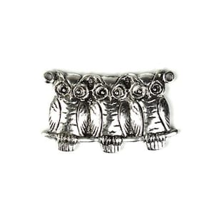 May include: Silver charm featuring four owls perched on a branch, with their wings spread out and their eyes wide open.