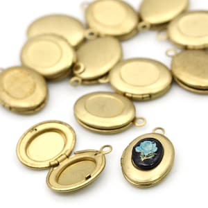 May include: A collection of small, oval-shaped, gold-colored lockets. Some lockets are closed, while others are open, revealing the interior. One locket features a blue rose design on a black background. The lockets have a loop for attaching a chain.