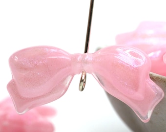 May include: Pink glitter bow charm with a silver loop. The bow is made of a translucent plastic material and has a sparkly finish.