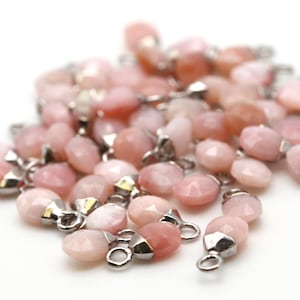 May include: A pile of pink opal gemstone beads with silver jump rings. The beads are faceted and have a pearlescent sheen.
