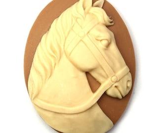 Puede incluir: Un camafeo beige con la cabeza de un caballo con una brida, sobre un fondo ovalado marrón.