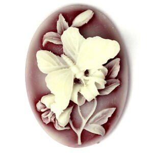 May include: An oval-shaped cameo with a white butterfly and floral design on a burgundy background.