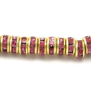 May include: A close-up of a strand of pink rhinestone beads with gold metal accents. The beads are round and have a smooth surface.