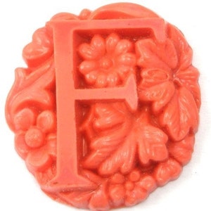 May include: A bright orange, floral-shaped resin letter F. The letter is raised and has a three-dimensional design.