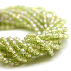 May include: A close-up of a strand of green iridescent glass beads. The beads are faceted and have a slightly irregular shape.