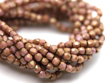May include: A coiled strand of small, faceted glass beads in a muted mauve and metallic bronze finish. Each bead features a multi-faceted surface that reflects light, creating a shimmering, textured appearance across the entire circular arrangement.