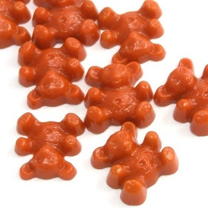 Puede incluir: Un grupo de diez pequeños ositos de goma naranja con forma de ositos de peluche. Los ositos de goma están dispuestos en un patrón aleatorio sobre un fondo blanco.