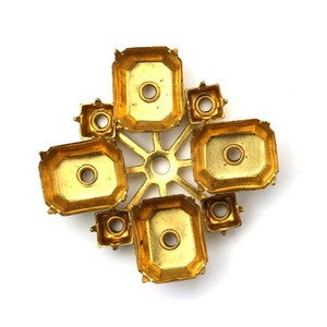 May include: Gold-toned metal setting with multiple open spaces for rhinestones or other embellishments. The setting is shaped like a cross with a central starburst design.