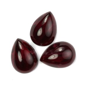 Pode incluir: Três contas de vidro em forma de lágrima com uma cor vermelho-escuro e um padrão de mármore em espiral. As contas têm um acabamento brilhante.