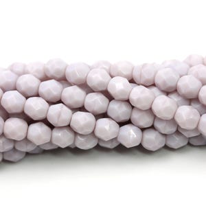 May include: A strand of pale lavender beads, each featuring a multifaceted, geometric cut. The beads are arranged in a dense, horizontal row, showcasing a consistent light purple hue and a smooth, reflective surface across their many angled facets.