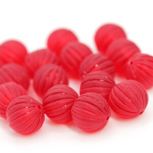 May include: A collection of red, ribbed beads. Each bead is round with a series of parallel grooves. The beads are a vibrant red color and appear to be made of a translucent material. The beads are scattered on a white background.