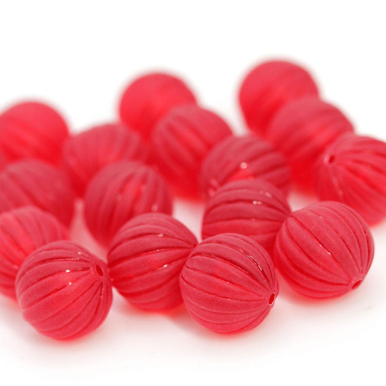 May include: A collection of red, ribbed beads. Each bead is round with a series of parallel grooves. The beads are a vibrant red color and appear to be made of a translucent material. The beads are scattered on a white background.