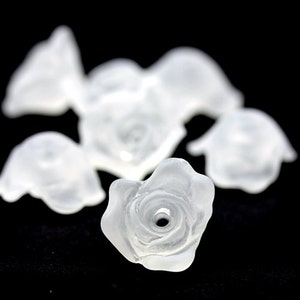 May include: A group of clear plastic rose-shaped beads. The beads are arranged in a cluster on a black background.