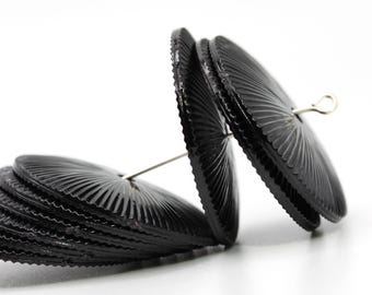 Könnte beinhalten: Nahaufnahme einer Sammlung schwarzer, kreisförmiger Perlen mit gerilltem, fächerförmigem Design. Die Perlen sind mit silberfarbenem Draht aufgefädelt und bilden eine einzigartige und künstlerische Anordnung. Die Perlen sind vor weißem Hintergrund.