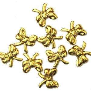 May include: Ten gold-colored metal bow embellishments. Each bow has a three-dimensional shape and is designed to be used as a decorative accent.