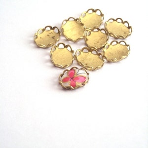 May include: A collection of eight gold-colored metal settings with scalloped edges, and one round, white cabochon with a pink floral design.