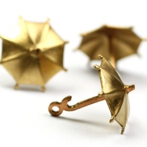 May include: Three miniature gold-colored umbrellas. Two are lying flat, while the third is standing upright with a handle.
