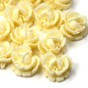 May include: A collection of small, white, sugar paste flower decorations. The flowers are in a rosette shape with a ruffled edge.