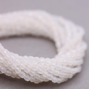 May include: A strand of white opaque glass beads. The beads are small and round with a slightly faceted surface.