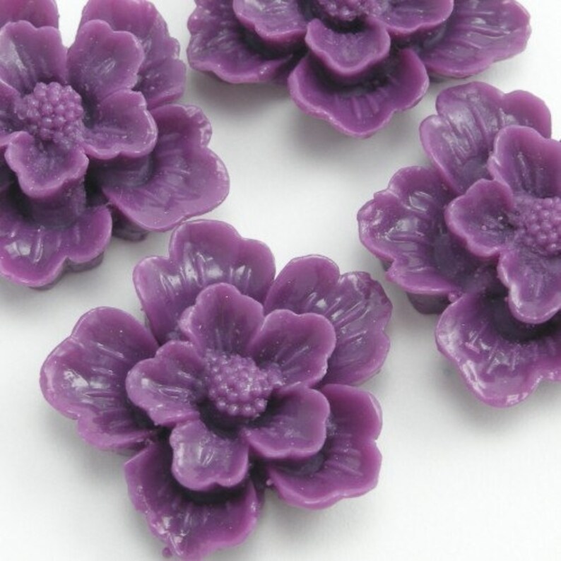 May include: Five purple resin flower cabochons. Each flower has five petals and a center with a textured design.